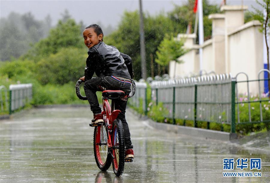 在吉隆县吉隆镇玛嘎村,一名儿童在享受雨中骑行的乐趣(7月26日摄).