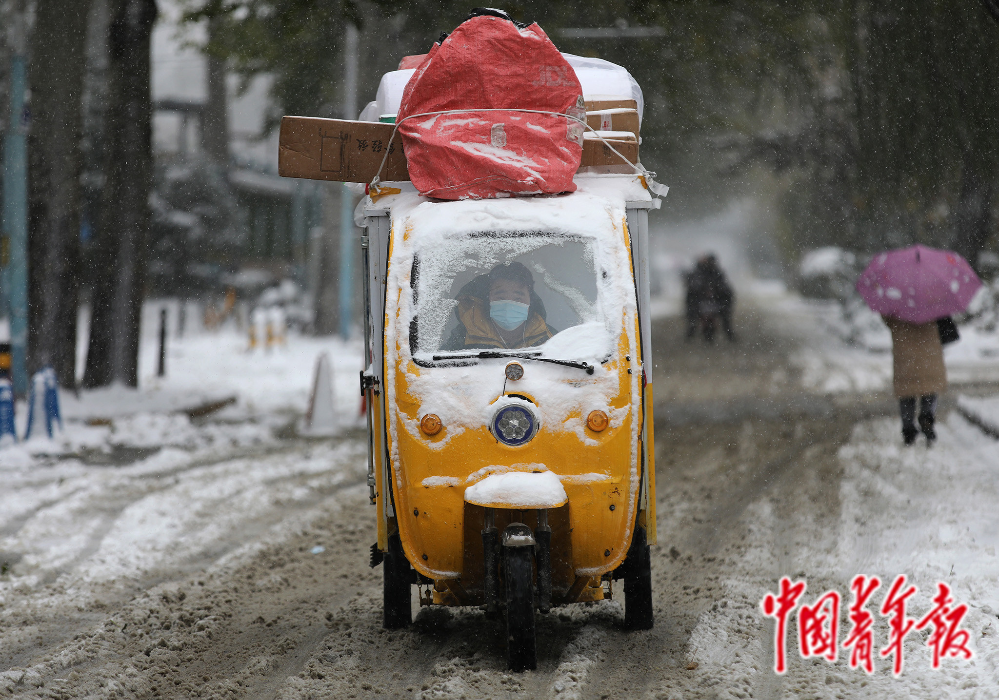 一名快递小哥驾驶着满载货物的电动三轮车在纷飞的大雪中前行